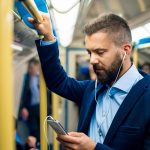 un homme qui tient la barre de metro et regarde son portable